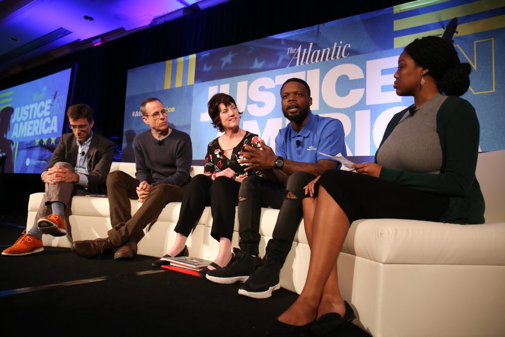 Panelists sitting on the stage in front of a "Justice in America" sign