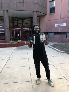 Jason Reynolds stands outside the DC jail holding copies of his books Long Way Down and When I Was the Greatest