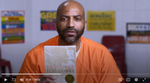 Free Minds member Rodney in an orange jumpsuit holds a copy of The Giver