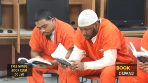 Two men in orange jumpsuits reading The Things They Carried