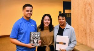 Three people stand in a row holding a book called The Untold Story of the Real Me