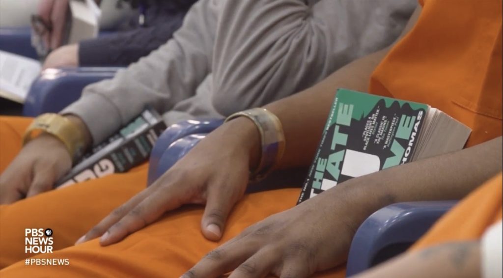 a man in an orange jumpsuit holding a book in his lap