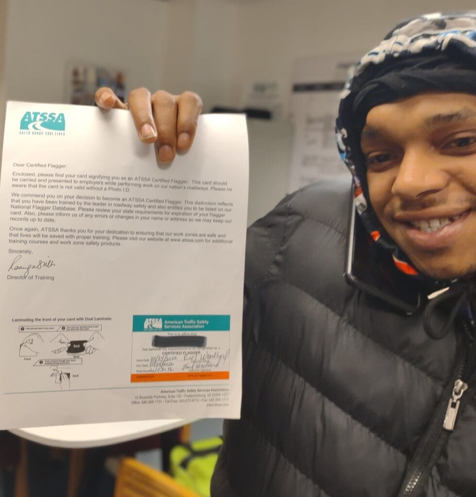 A smiling young man in a winter coat and hat, holding up a certificate