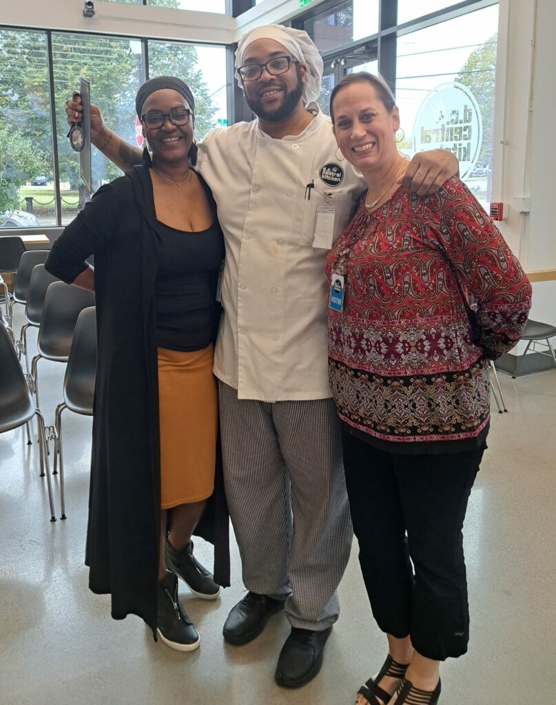 A man in a white chef's coat and hat stands smiling between two women.