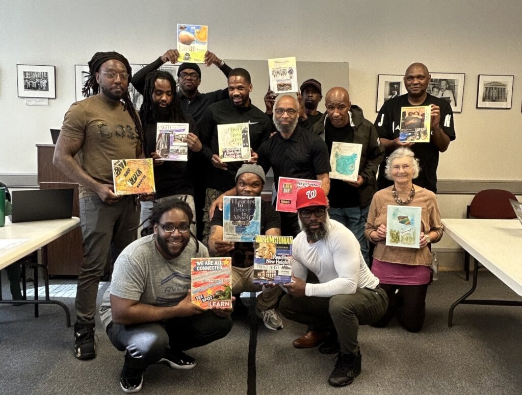 A group of men standing together each holding a colorful vision board.